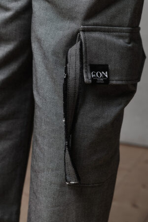 Ein Detailfoto des rechten Beines einer Jeanshose. Im Mittelpunkt steht eine aufgenähte Tasche mit Band und einem Etikett mit Logo.