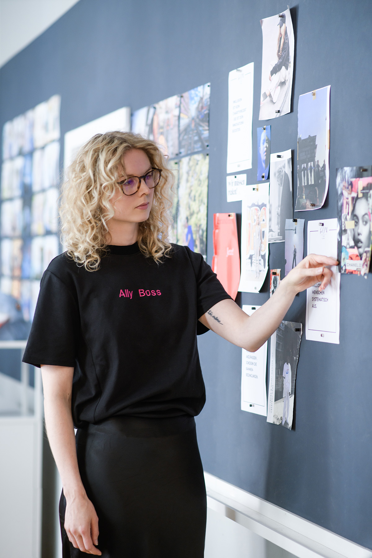eine blonde Frau mit Locken - Claire Common bei der Arbeit - "Ally Boss" Shirt, Moodboard mit inklusiven Modeentwürfen